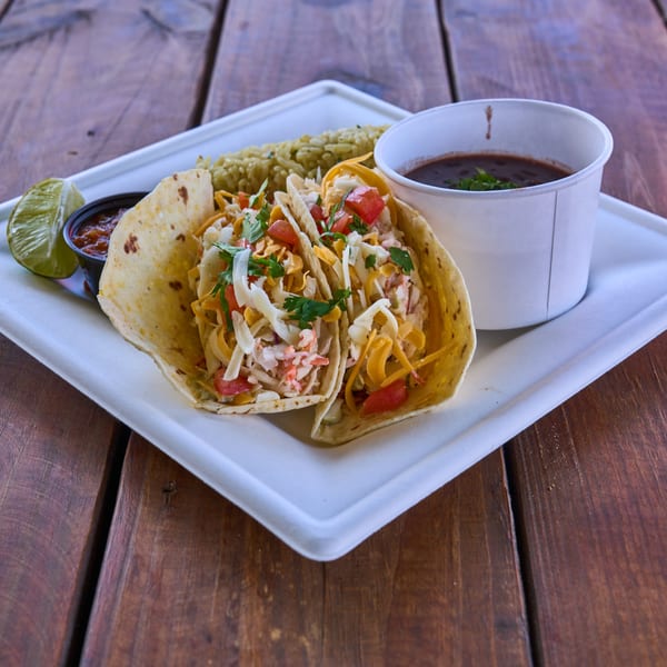 Two soft tacos with shredded cheese, tomatoes, and cilantro, served with rice and black beans.