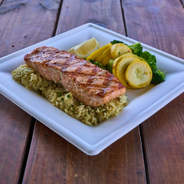 Grilled salmon fillet with rice, broccoli, yellow squash, and a lemon wedge on a white plate.