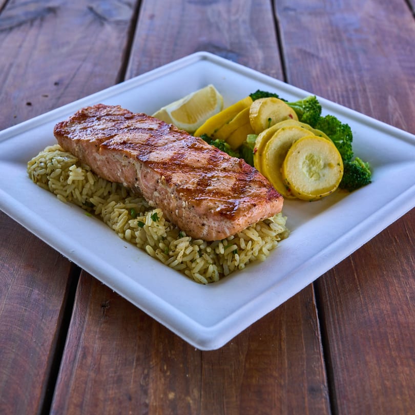 Grilled salmon fillet with rice, broccoli, yellow squash, and a lemon wedge on a white plate.