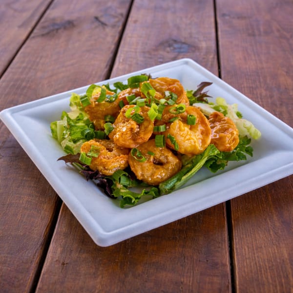 Crispy shrimp coated in orange sauce, garnished with green onions and served on a bed of lettuce.