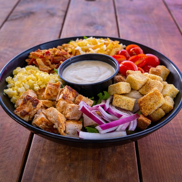 A black bowl filled with a salad featuring chicken, tomatoes, croutons, cheese, and dressing.
