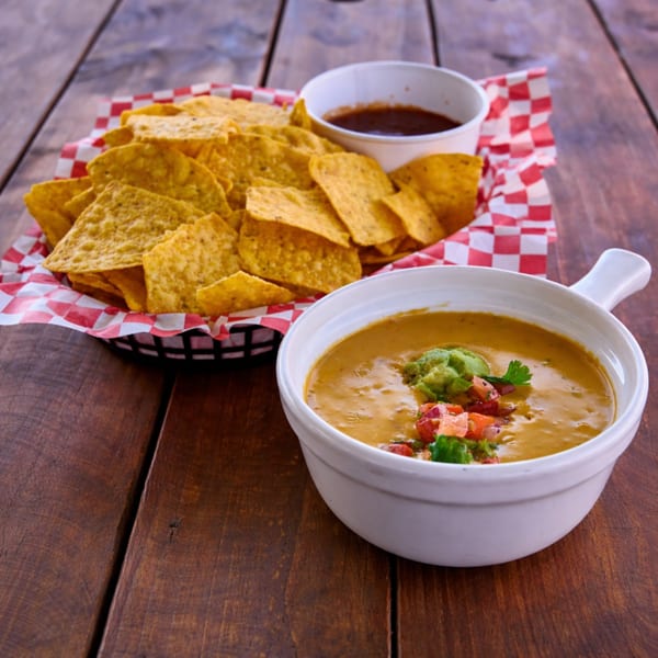 Nachos with cheese dip topped with guacamole and salsa, and a side of salsa on a wooden table.