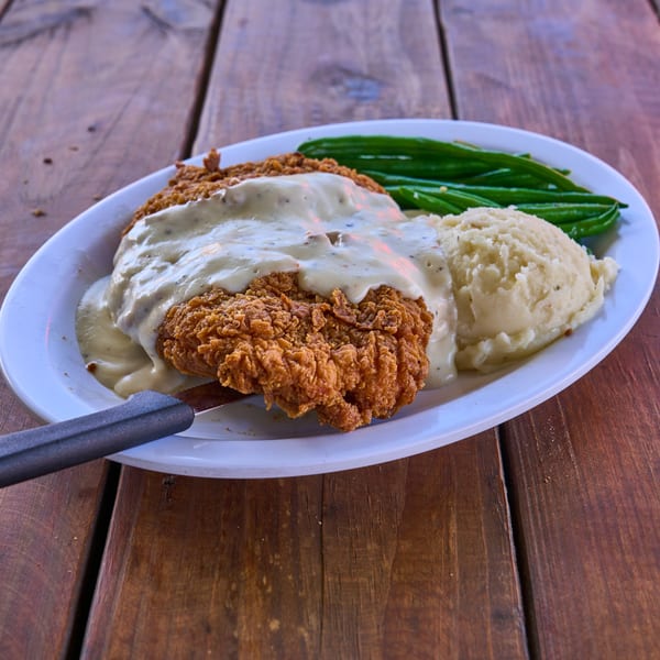Crispy chicken fried steak with gravy, mashed potatoes, and green beans on a white plate.