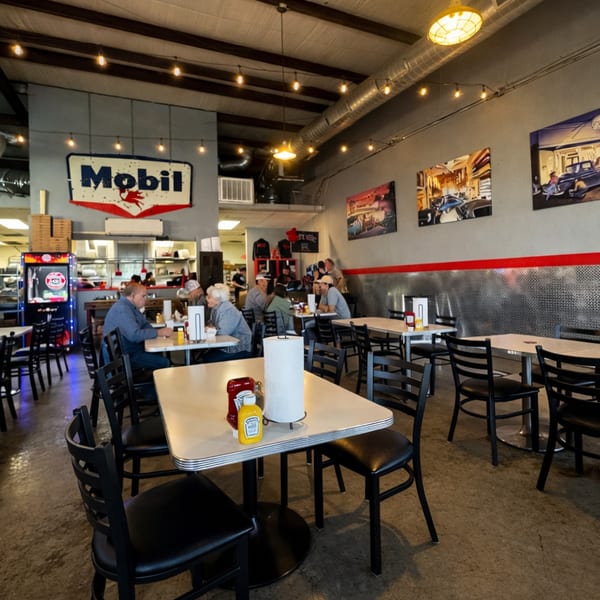 Diners seated at tables in a casual restaurant with a Mobil sign and car-themed artwork.