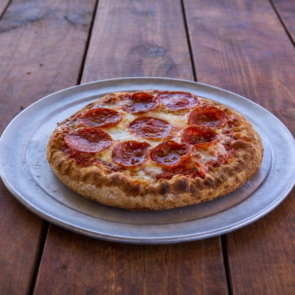 A small, round pepperoni pizza with melted cheese on a metal tray, on a wooden table.